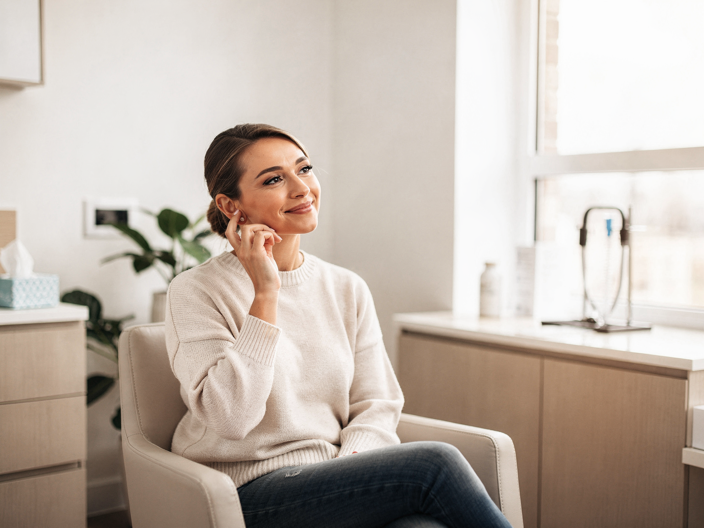 Woman sitting in a modern medical office waiting room with light wood cabinetry and plants